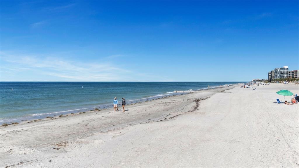 A wide, sandy beach stretches along the ocean under a clear blue sky — 14900 GULF BOULEVARD UNIT 410, MADEIRA BEACH, FL