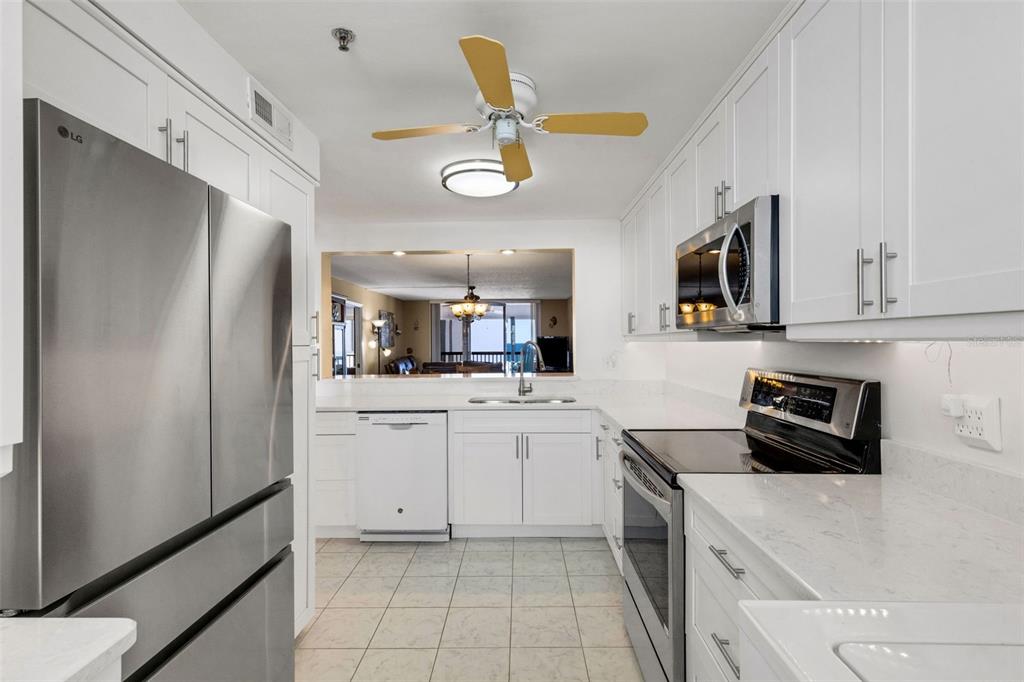 A kitchen with white cabinets, stainless steel appliances, and a pass-through window to the living area — 14900 GULF BOULEVARD UNIT 410, MADEIRA BEACH, FL