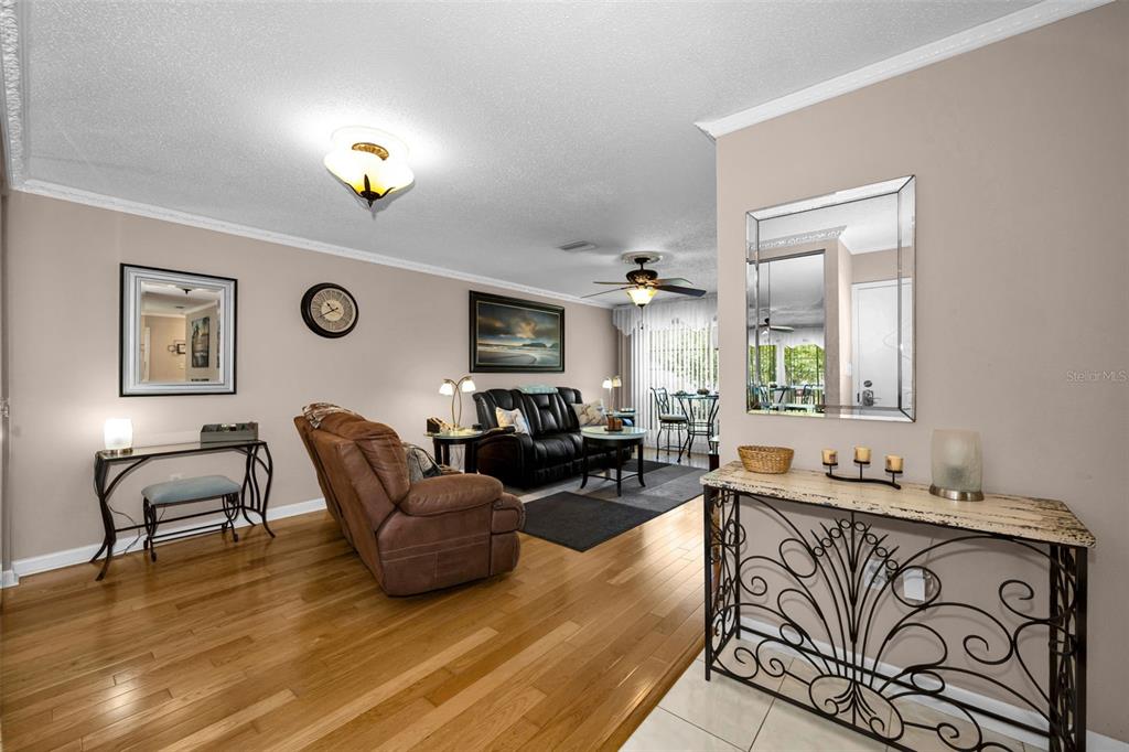 A living room features hardwood floors, a brown recliner, a black sofa, and decorative consoles — 2700 BAYSHORE BOULEVARD UNIT 2205, DUNEDIN, FL