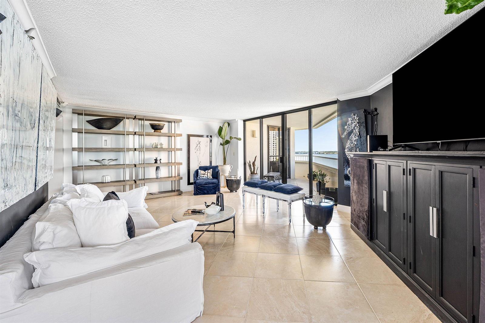 A bright living room features a white sofa, open shelving, and sliding doors to a balcony — 5080 N Ocean Drive # 6b, Singer Island FL 33404, SINGER ISLAND, FL