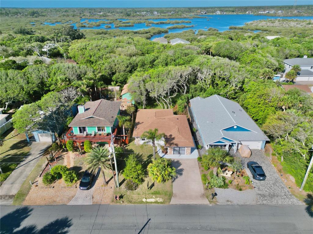 An aerial view shows three houses along a road with dense trees and a waterway behind — 1624 S DAYTONA AVENUE, FLAGLER BEACH, FL