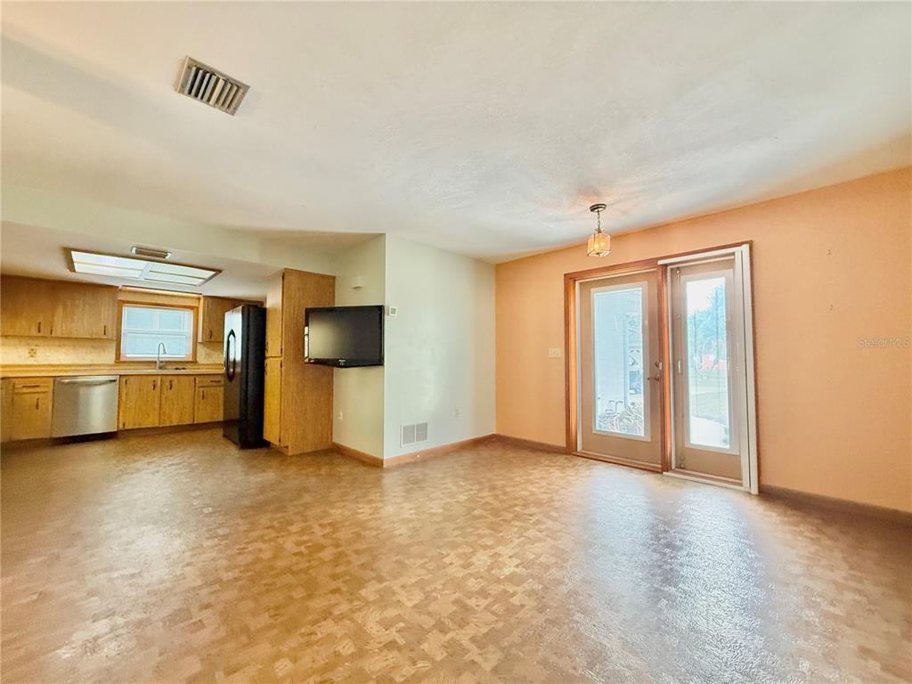 An open-concept kitchen and dining area features wood cabinets, vinyl flooring, and glass sliding doors — 1624 S DAYTONA AVENUE, FLAGLER BEACH, FL
