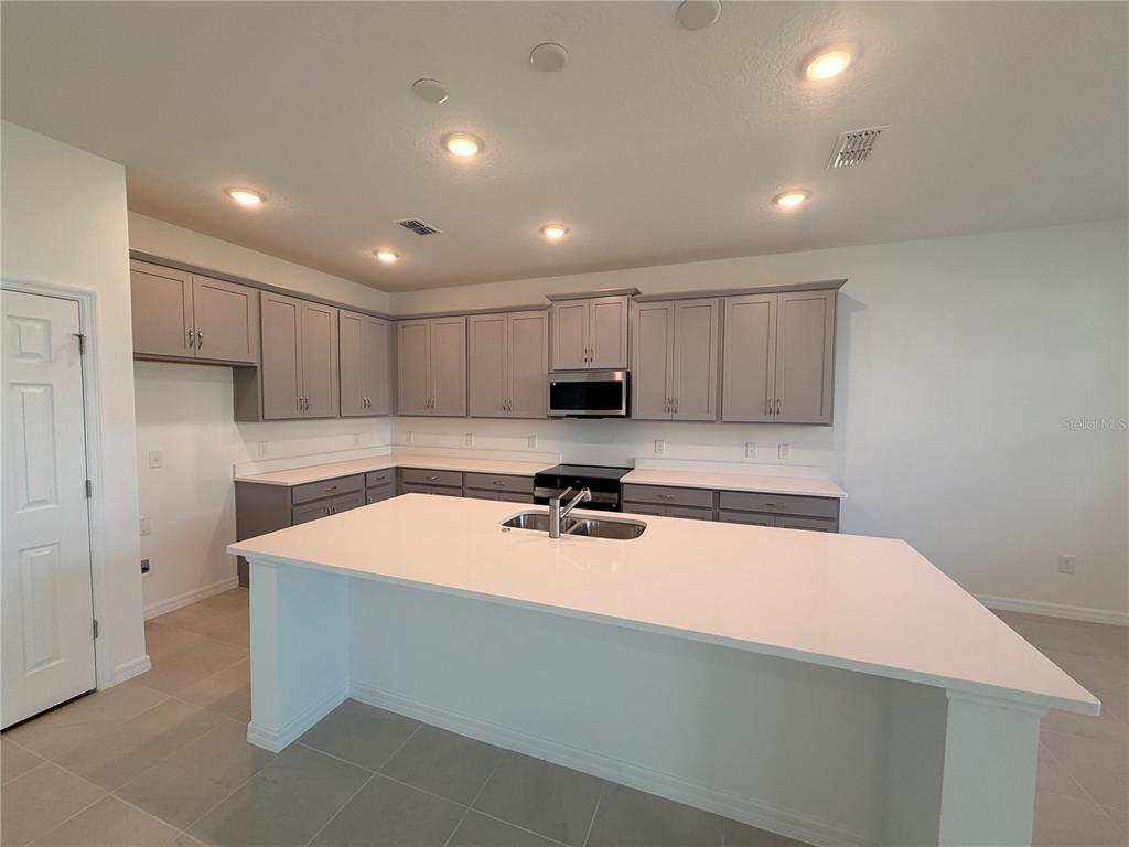 A modern kitchen features gray cabinets, a large white island, and light-colored tile flooring — 2011 EDUCATION STREET, ST CLOUD, FL