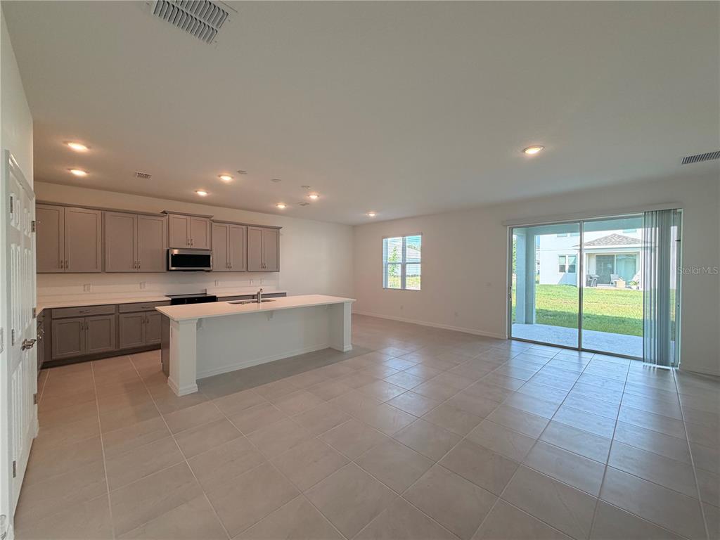 An open-concept kitchen and living area features gray cabinets, a white island, and tile flooring — 2011 EDUCATION STREET, ST CLOUD, FL