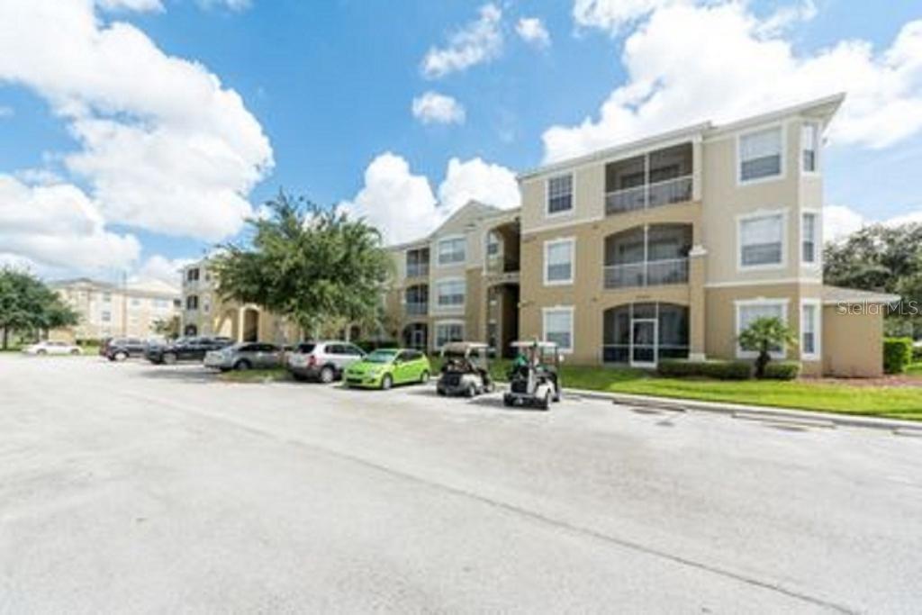 A multi-story apartment building with tan stucco siding and screened balconies sits near a parking lot — 2781 ALMATON LOOP UNIT 304, KISSIMMEE, FL
