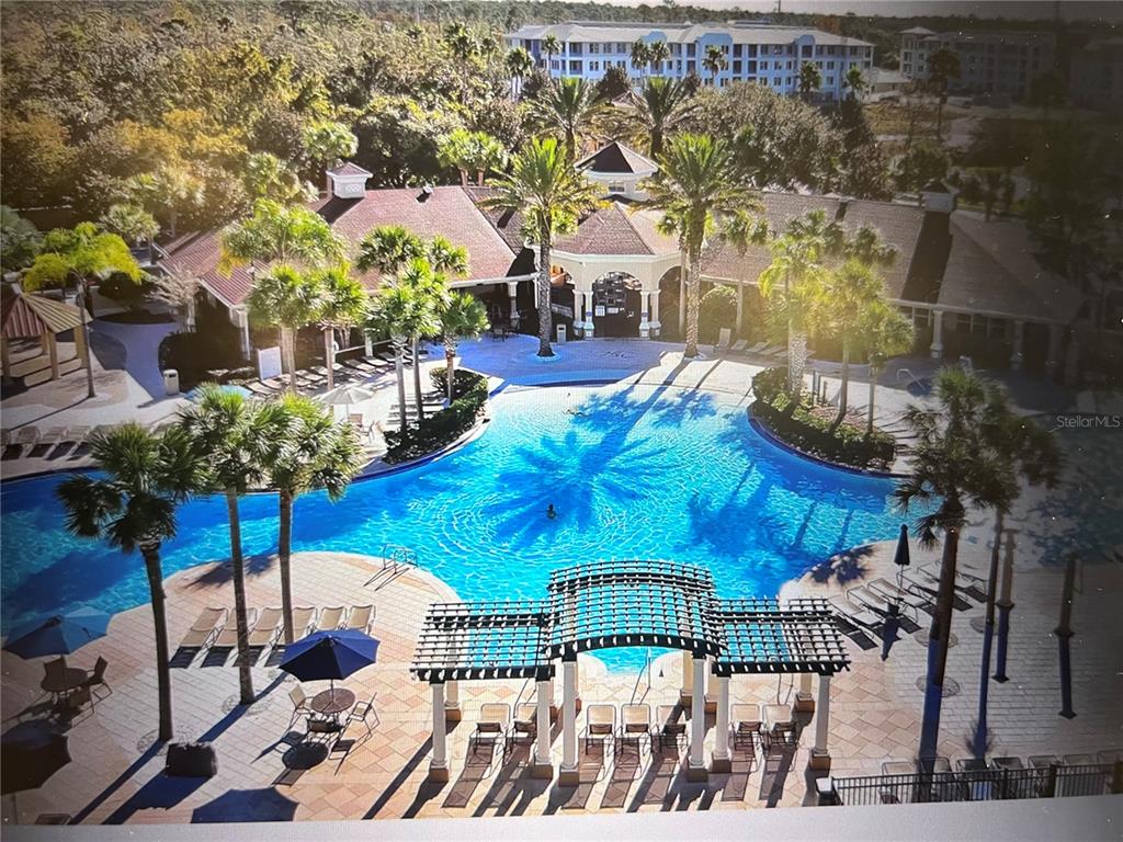 An aerial view of a resort-style swimming pool surrounded by a patio, palm trees, and buildings — 2781 ALMATON LOOP UNIT 304, KISSIMMEE, FL
