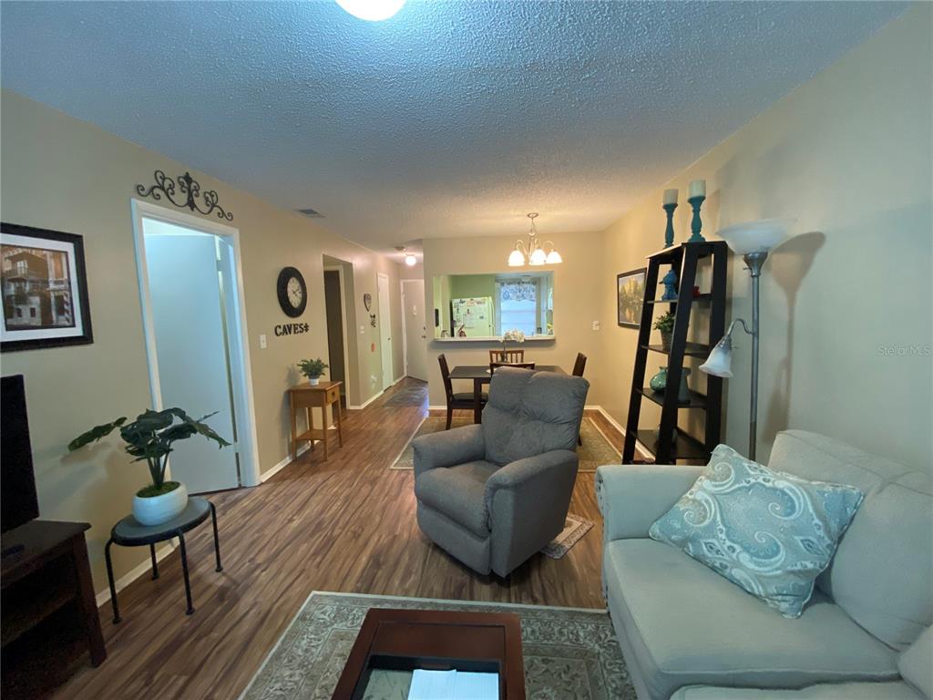 A living room with wood-look flooring leads to a dining area with a pass-through window — 9609 MIDIRON COURT UNIT 1, NEW PORT RICHEY, FL