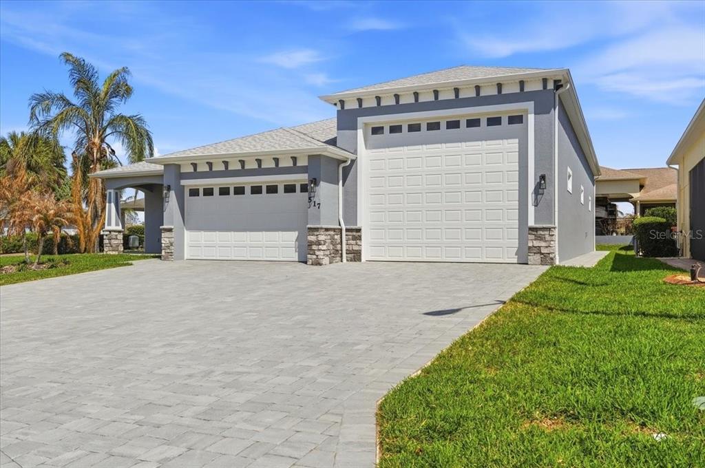 A gray house with a three-car garage and a paved driveway under a blue sky — 517 HOME COMING WAY, POLK CITY, FL