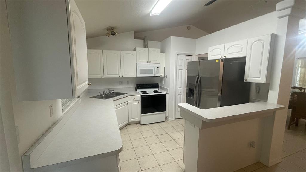 A kitchen features white cabinets, light countertops, stainless steel appliances, and tile flooring — 32 ALMOND DRIVE, OCALA, FL