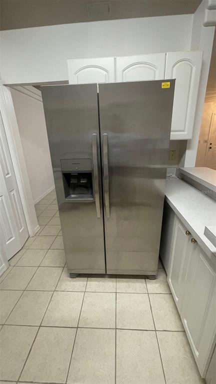 A stainless steel side-by-side refrigerator stands in a kitchen with white cabinets and tile flooring — 32 ALMOND DRIVE, OCALA, FL