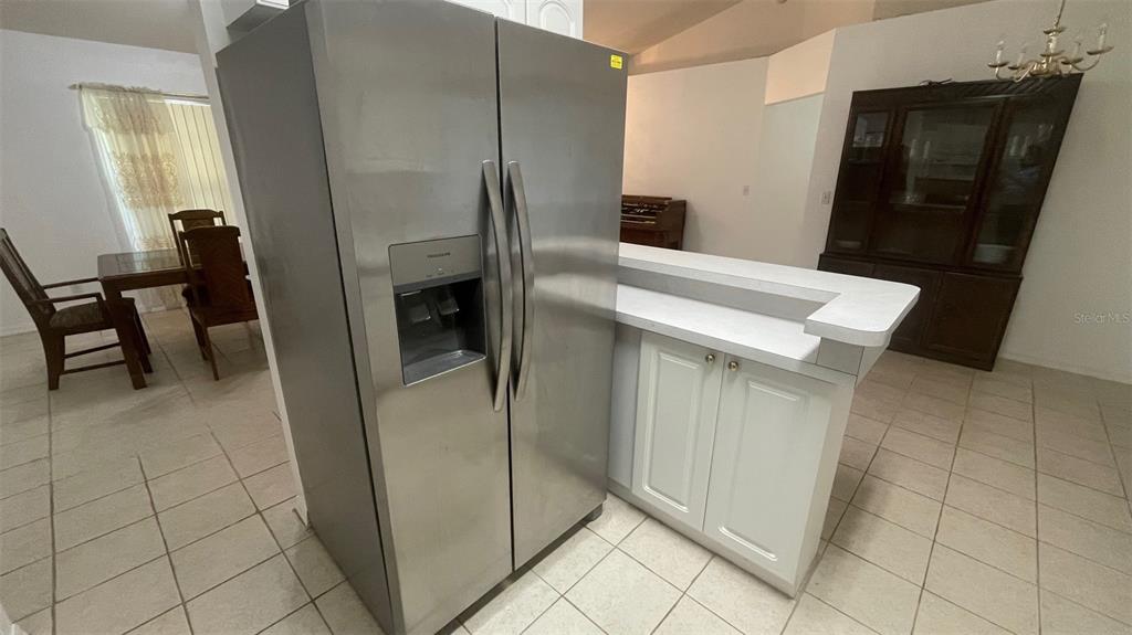 A stainless steel refrigerator stands next to a white kitchen island with tiled flooring — 32 ALMOND DRIVE, OCALA, FL