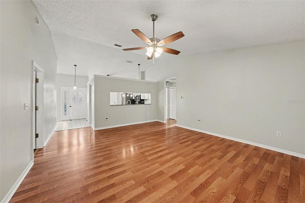 An open living room features wood flooring, a vaulted ceiling with a fan, and a pass-through — 8116 MATTHEW DRIVE, NEW PORT RICHEY, FL
