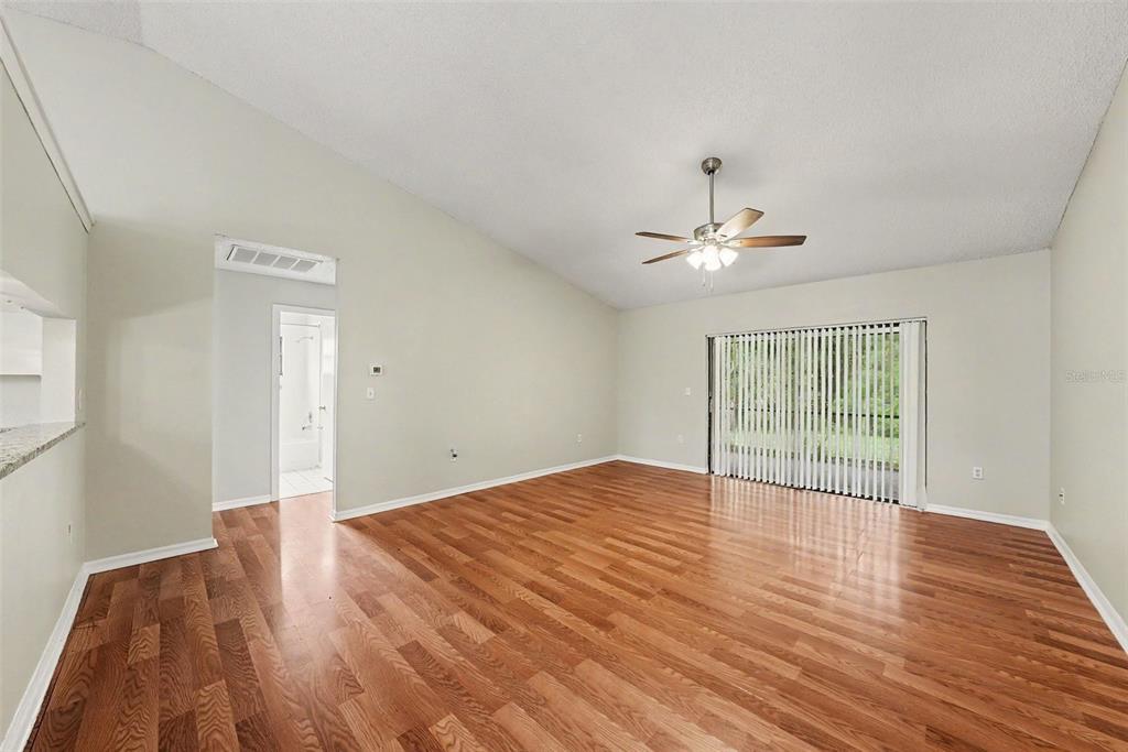 An empty living room features hardwood floors, a ceiling fan, and sliding glass patio doors — 8116 MATTHEW DRIVE, NEW PORT RICHEY, FL