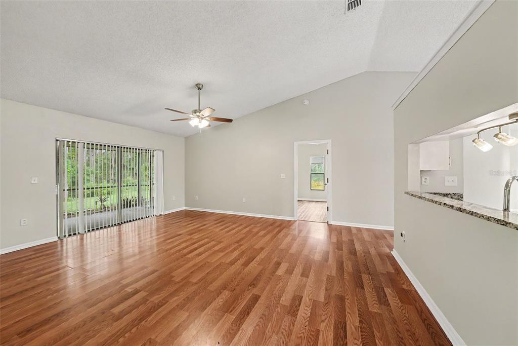 An empty living room with vaulted ceilings, wood-look flooring, and a sliding glass door — 8116 MATTHEW DRIVE, NEW PORT RICHEY, FL
