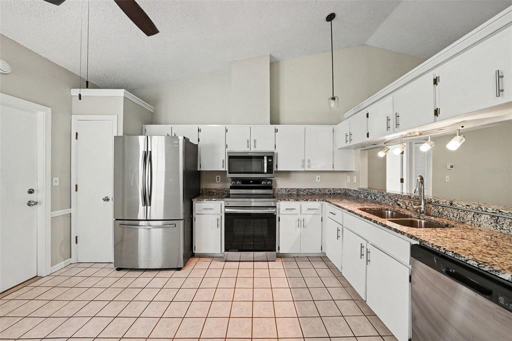 A kitchen with white cabinets, granite countertops, stainless steel appliances, and light-colored tile flooring — 8116 MATTHEW DRIVE, NEW PORT RICHEY, FL
