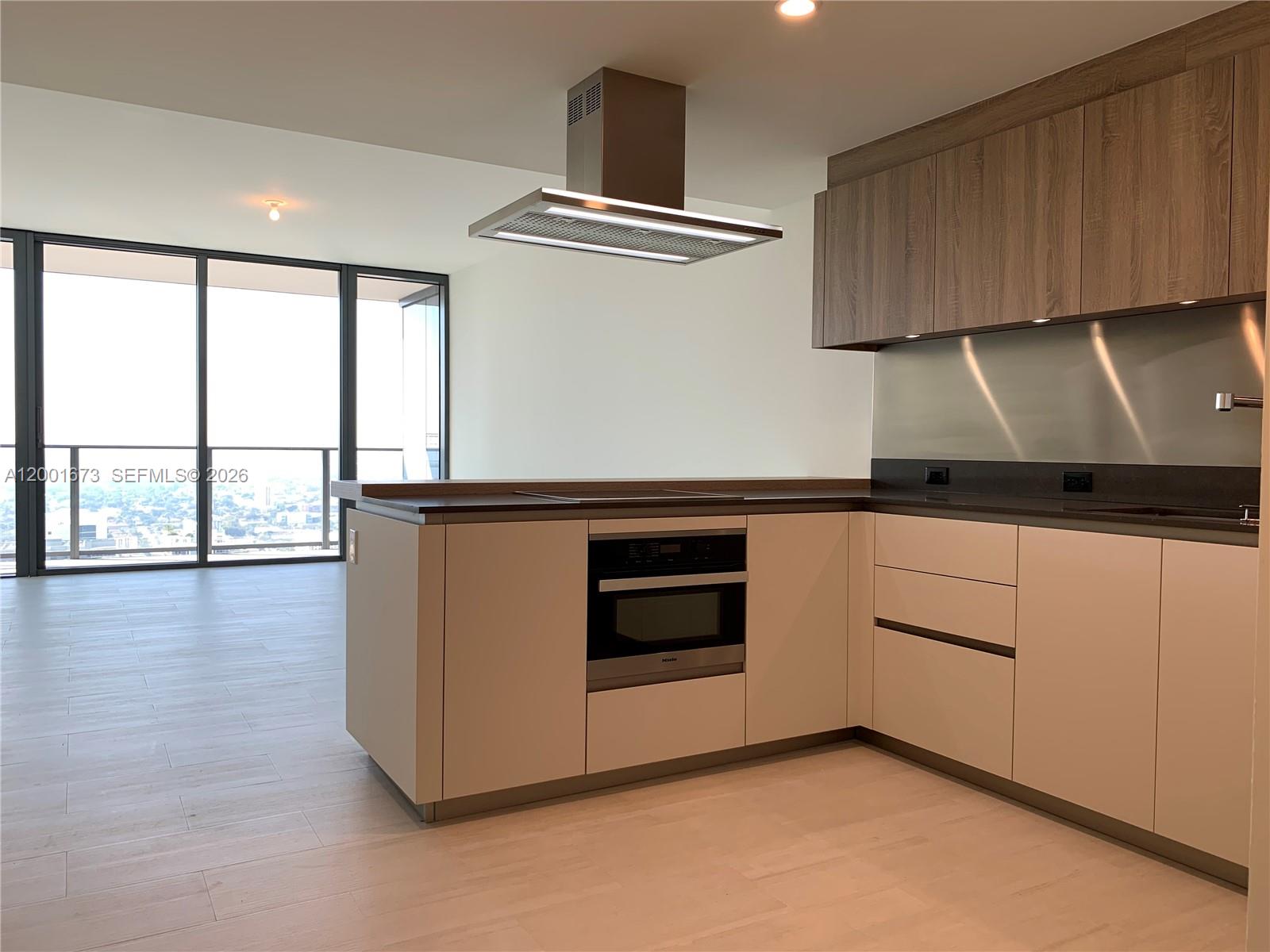A modern kitchen features light-colored cabinetry, a stainless steel range hood, and floor-to-ceiling windows — 1000 Brickell Plz # 3904, Miami FL 33131, MIAMI, FL