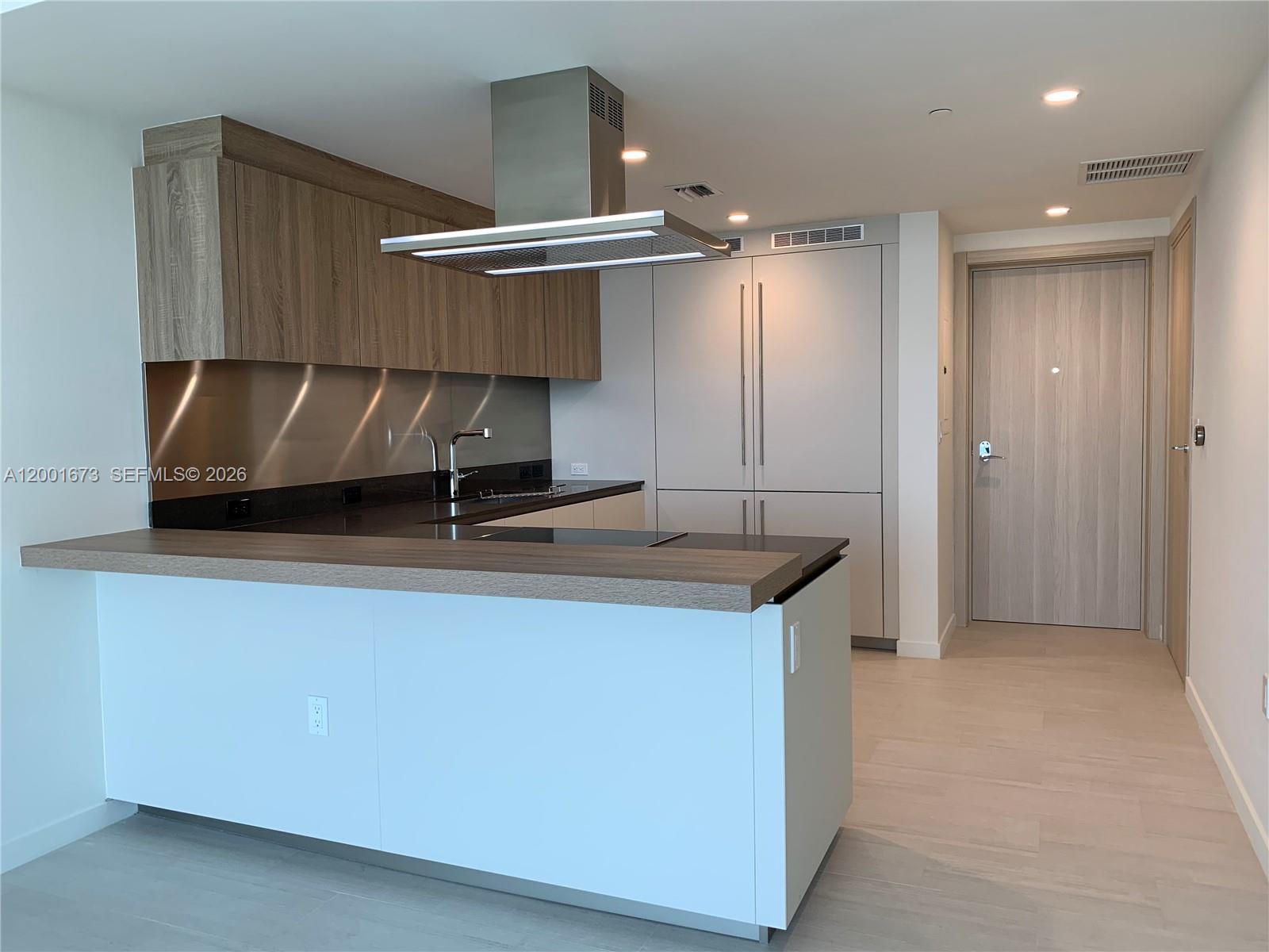 A modern kitchen features wood-tone upper cabinets, a stainless steel range hood, and a peninsula — 1000 Brickell Plz # 3904, Miami FL 33131, MIAMI, FL