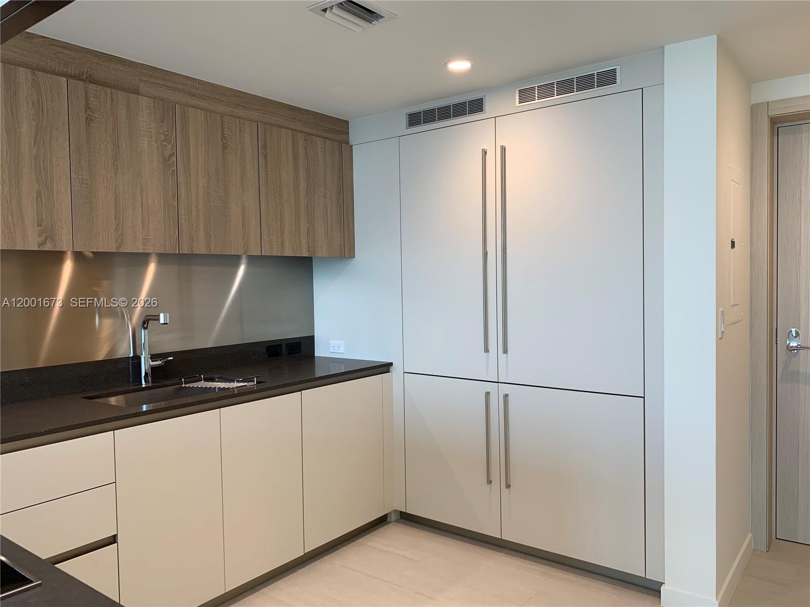 A modern kitchen features wood-grain upper cabinets, white lower cabinets, and integrated stainless steel appliances — 1000 Brickell Plz # 3904, Miami FL 33131, MIAMI, FL