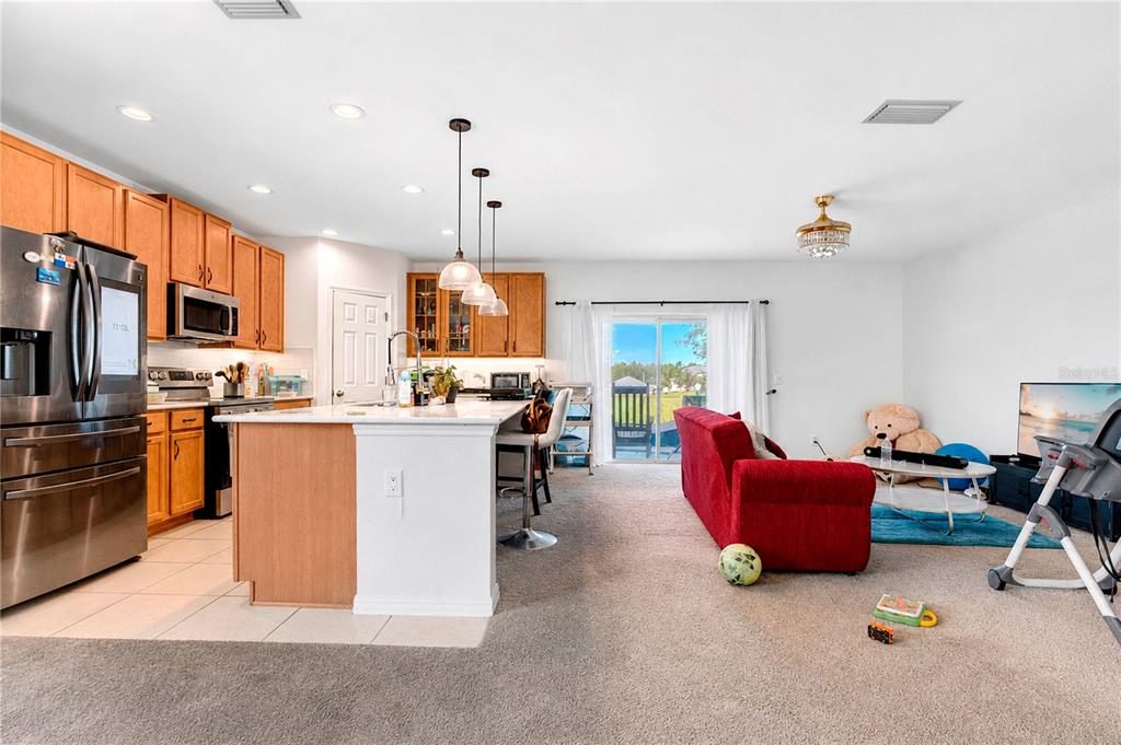 An open-concept kitchen with wood cabinets and an island flows into a carpeted living area — 449 TORTUGAS STREET, HAINES CITY, FL