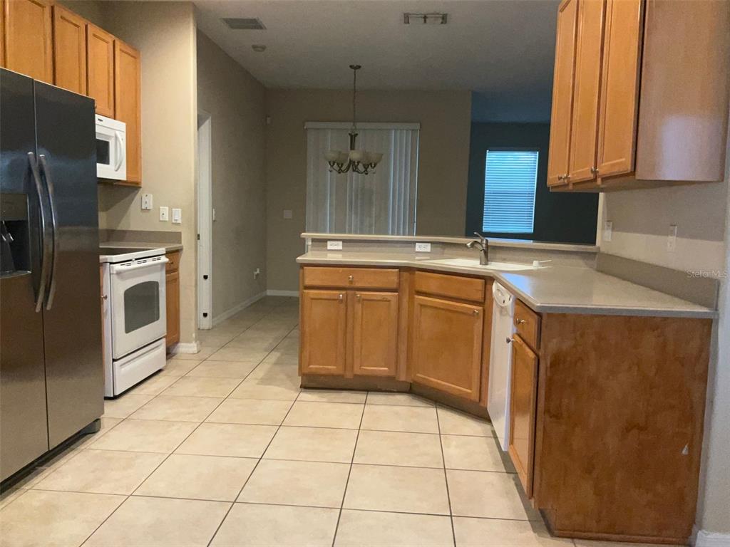 A kitchen features light wood cabinets, beige countertops, tile flooring, and stainless steel appliances — 5303 CAPE HATTERAS DRIVE, CLERMONT, FL