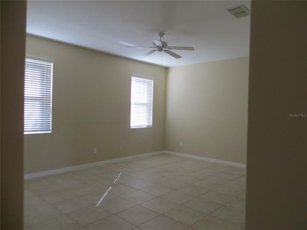 An empty room features beige walls, light-colored tile flooring, two windows with blinds, and a ceiling fan — 5303 CAPE HATTERAS DRIVE, CLERMONT, FL