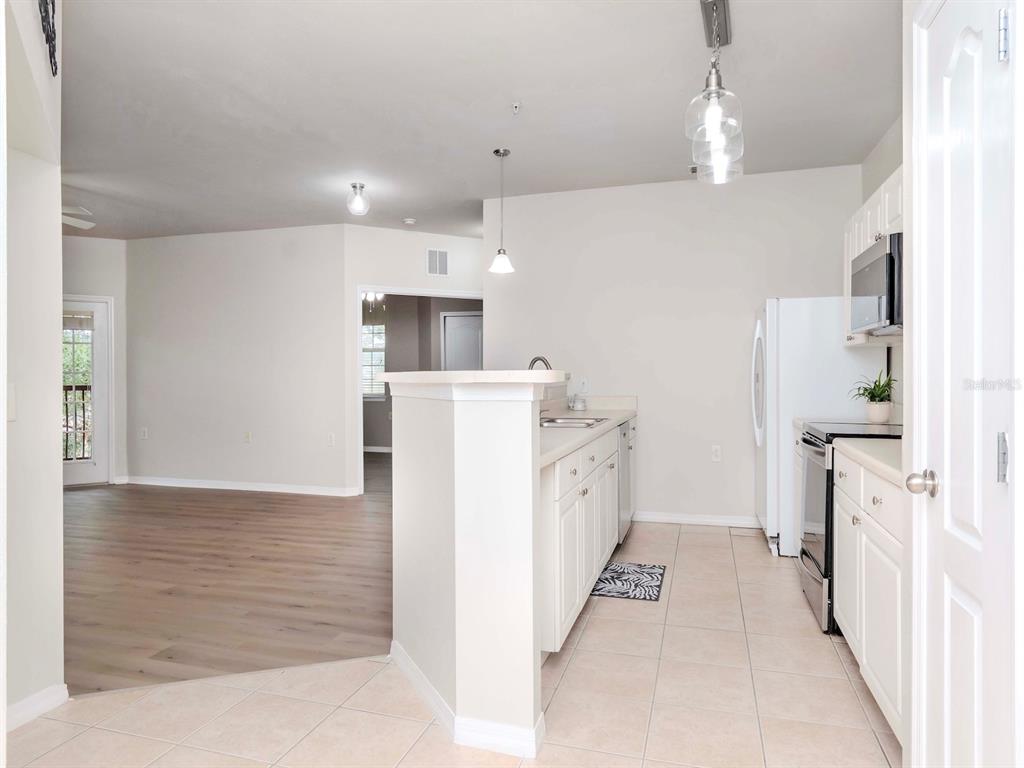 A kitchen with white cabinets and tile flooring opens to a living area with wood floors — 1429 VILLA CAPRI CIRCLE UNIT 306, ODESSA, FL