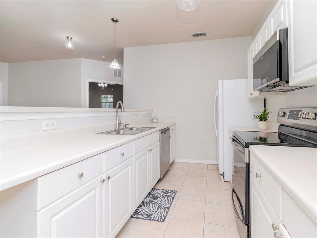 A kitchen features white cabinets, white countertops, stainless steel appliances, and light-colored tile flooring — 1429 VILLA CAPRI CIRCLE UNIT 306, ODESSA, FL