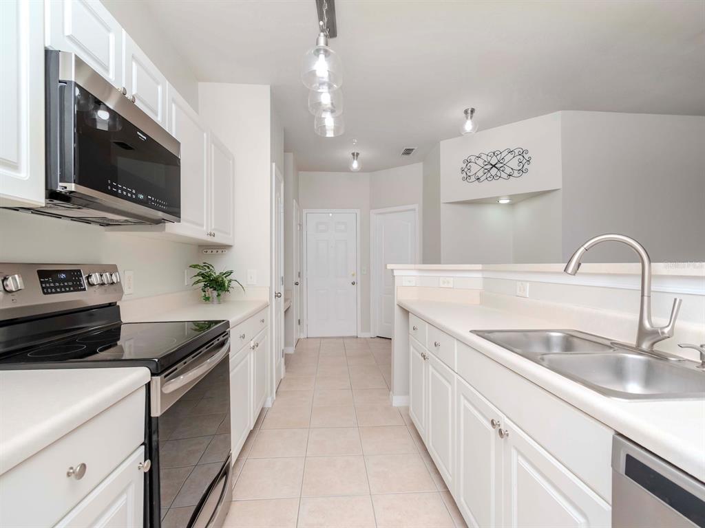 A galley kitchen features white cabinets, stainless steel appliances, a double sink, and tile flooring — 1429 VILLA CAPRI CIRCLE UNIT 306, ODESSA, FL