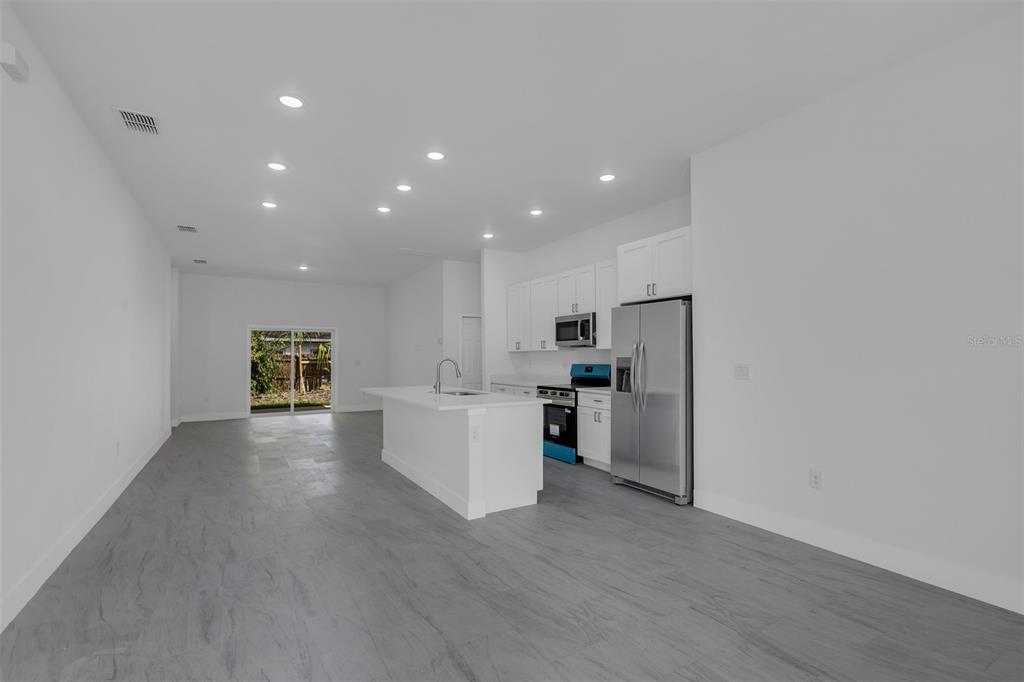 A modern kitchen with white cabinets and an island opens into a spacious living area — 1221 SW 5TH STREET, OCALA, FL