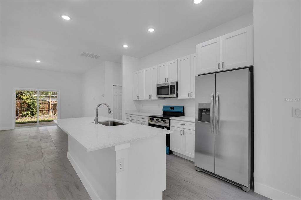 A modern kitchen features white cabinets, stainless steel appliances, a quartz island, and tile flooring — 1221 SW 5TH STREET, OCALA, FL