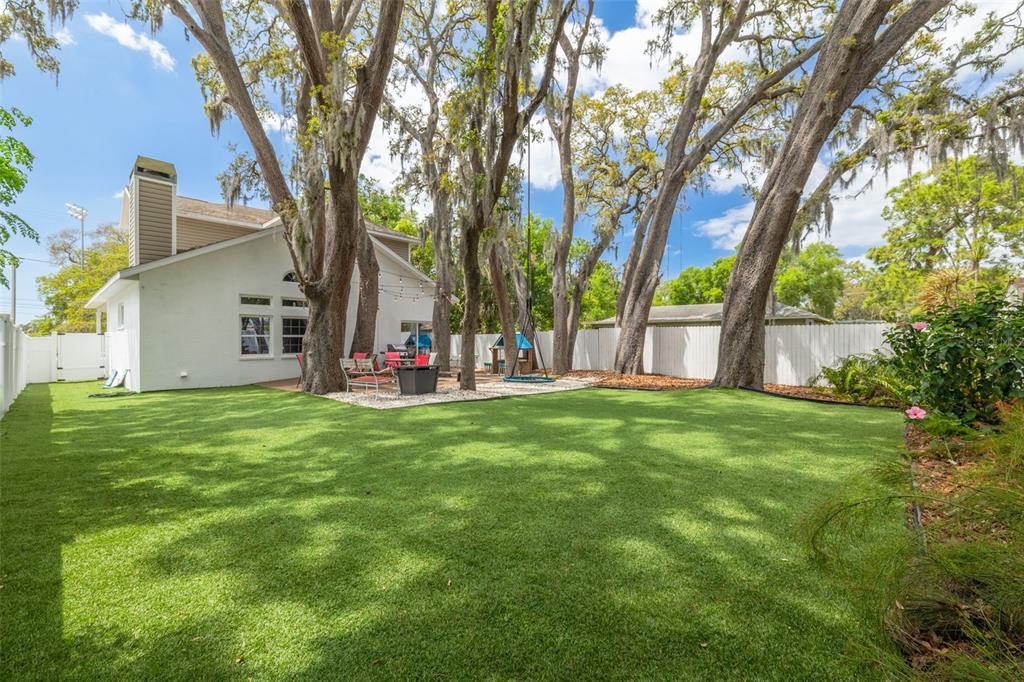 A backyard with artificial turf, large oak trees, a patio area, and a white fence — 901 VIRGINIA AVENUE, TARPON SPRINGS, FL