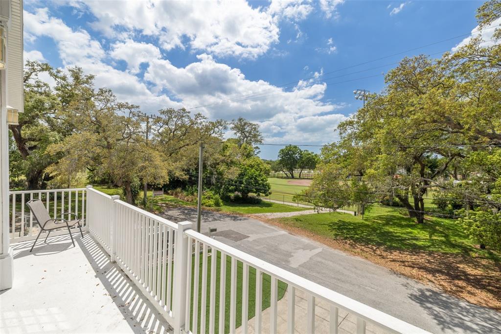 A white balcony overlooks a paved road, green trees, and a baseball field — 901 VIRGINIA AVENUE, TARPON SPRINGS, FL