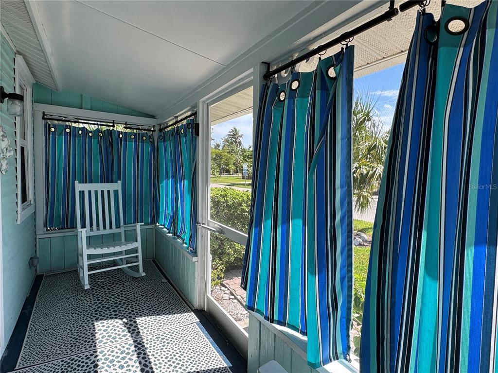 A screened-in porch features a white rocking chair, patterned floor mats, and blue striped curtains — 6980 POINSETTA, LONGBOAT KEY, FL