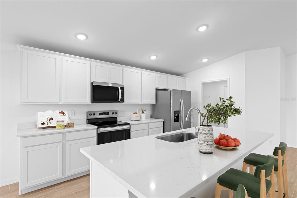 A modern kitchen features white cabinetry, a large quartz island, and stainless steel appliances — 23145 MCBURNEY AVENUE, PORT CHARLOTTE, FL