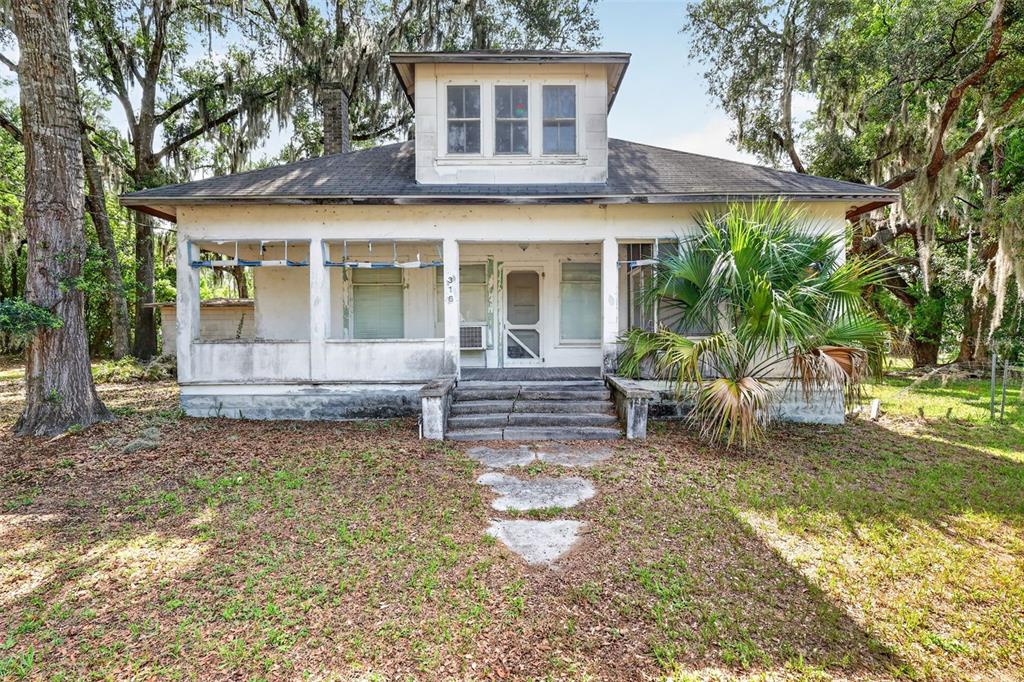 A weathered, single-story house with a front porch, dormer window, and stone walkway — 316 N HIGHLAND STREET, MOUNT DORA, FL