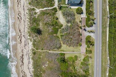 An aerial view shows a coastal property with a beach path, vegetation, and a driveway — FORT PIERCE, FL