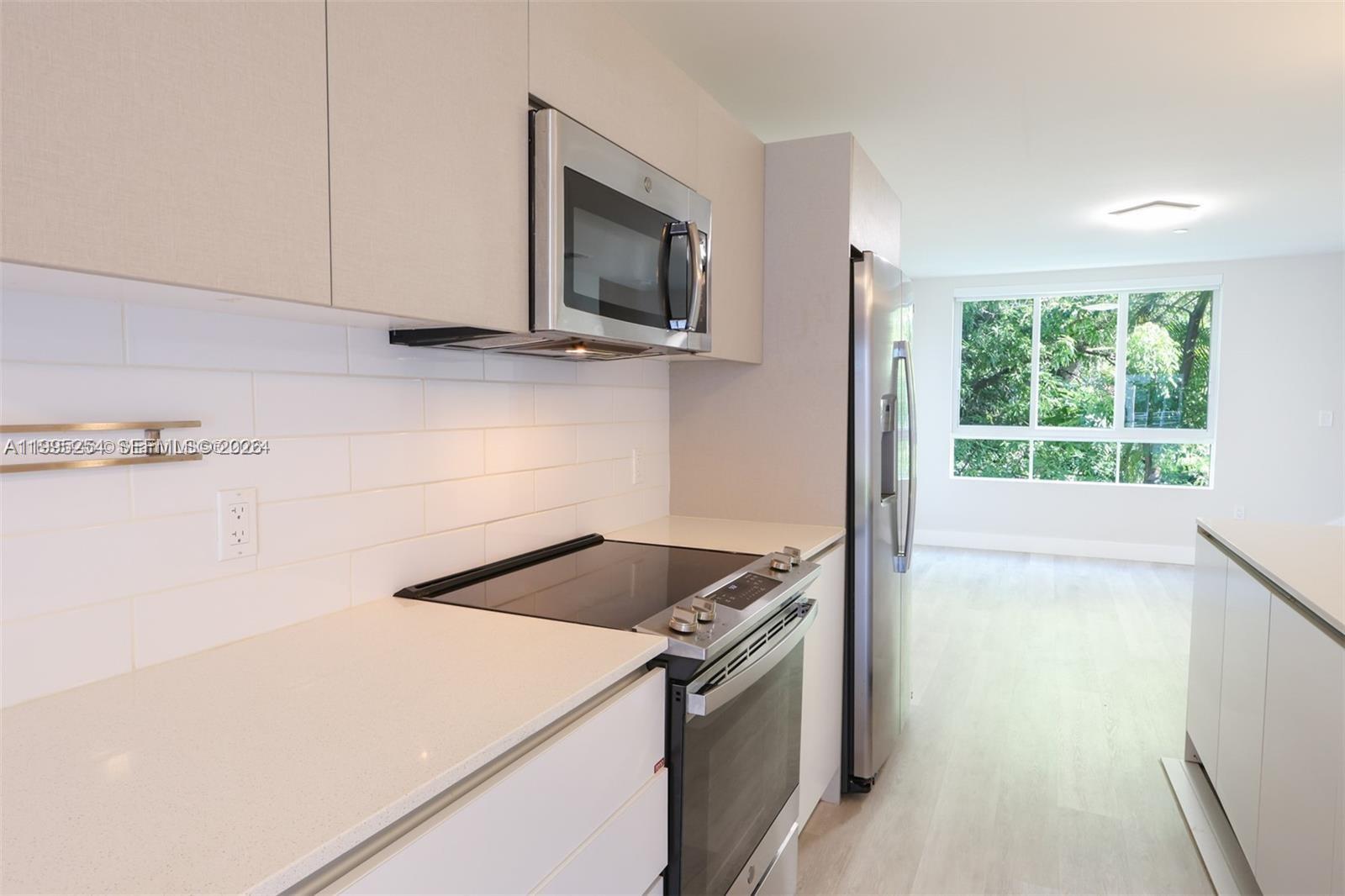 A modern kitchen features white cabinetry, stainless steel appliances, and a view of trees outside — 2555 NE 193rd St # 2206, Miami FL 33180, MIAMI, FL