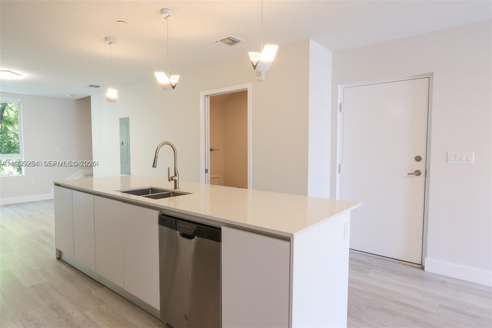 A modern kitchen features a white island with a stainless steel dishwasher and sink — 2555 NE 193rd St # 2206, Miami FL 33180, MIAMI, FL
