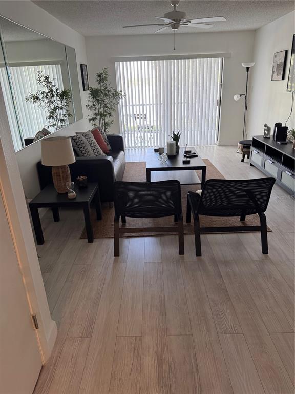A living room features light wood flooring, a black sofa, two mesh chairs, and vertical blinds — 2225 HOLDEN AVENUE UNIT 104, ORLANDO, FL