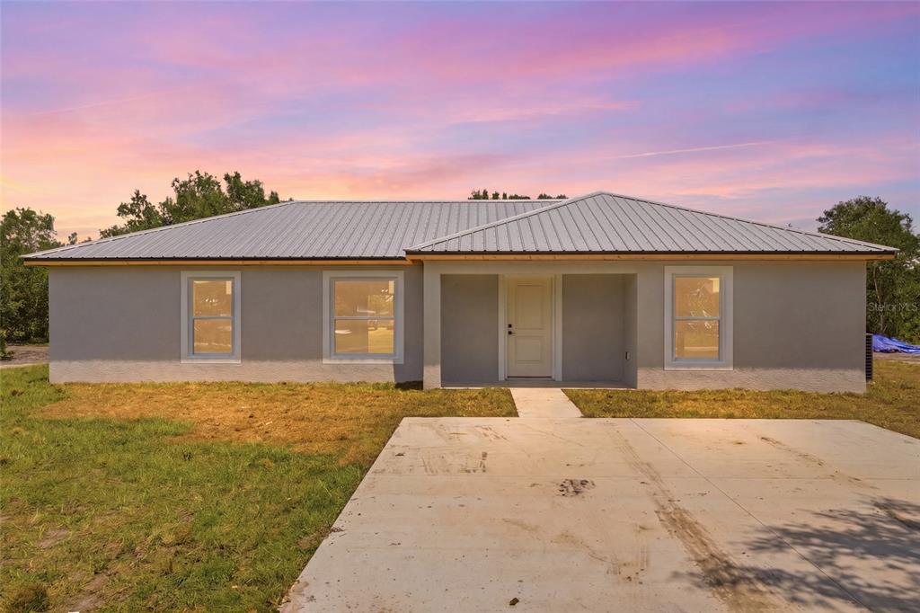 A single-story house with a gray stucco exterior, metal roof, and a concrete driveway — 6898 SW MIAMI AVENUE, ARCADIA, FL