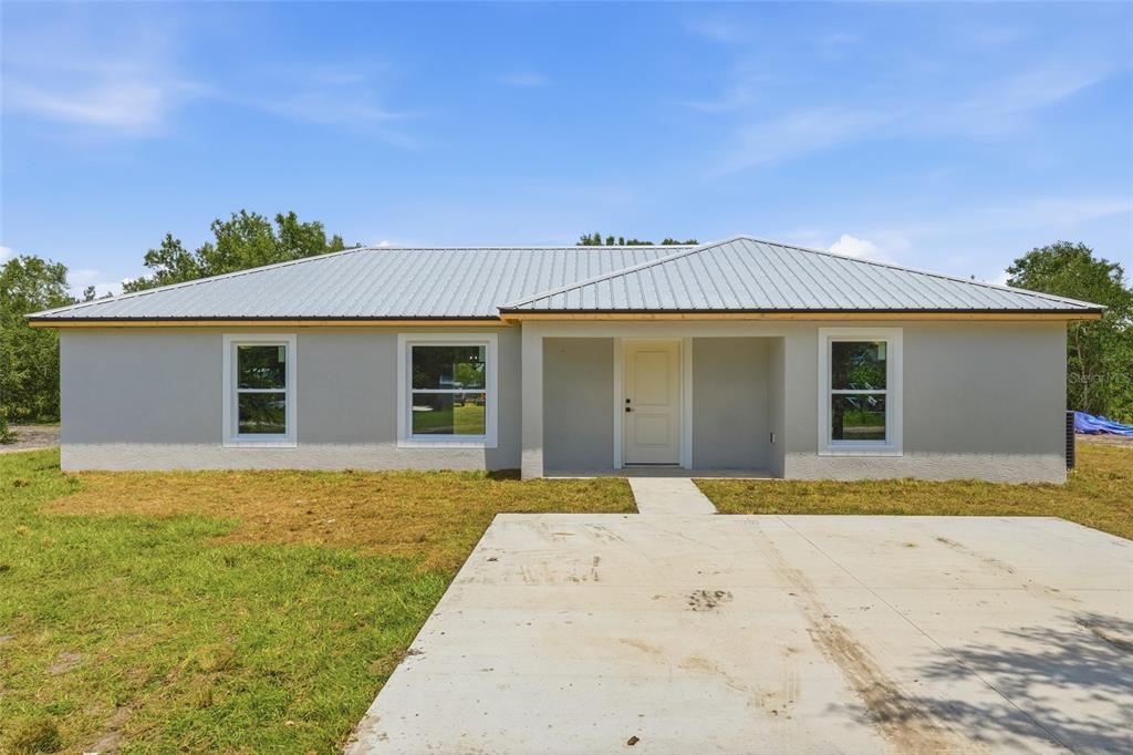 A single-story house with a gray stucco exterior, metal roof, and a concrete driveway — 6898 SW MIAMI AVENUE, ARCADIA, FL