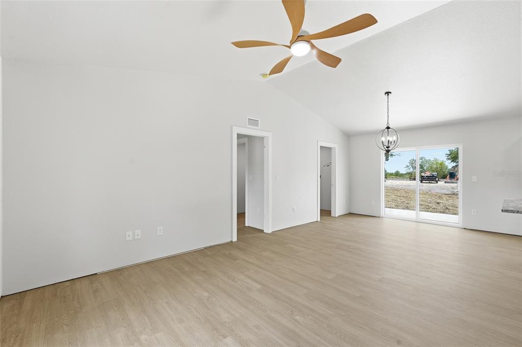 A bright, empty room features light wood-look flooring, a ceiling fan, and sliding glass doors — 6898 SW MIAMI AVENUE, ARCADIA, FL