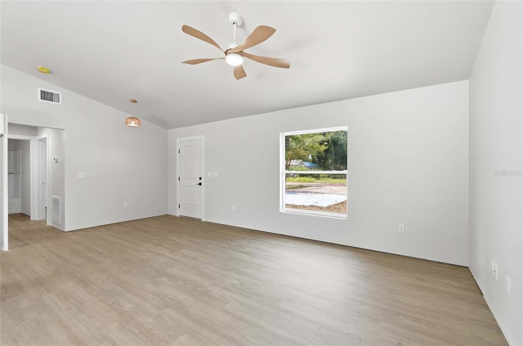 A bright, empty room features light wood-look flooring, white walls, a ceiling fan, and a window — 6898 SW MIAMI AVENUE, ARCADIA, FL