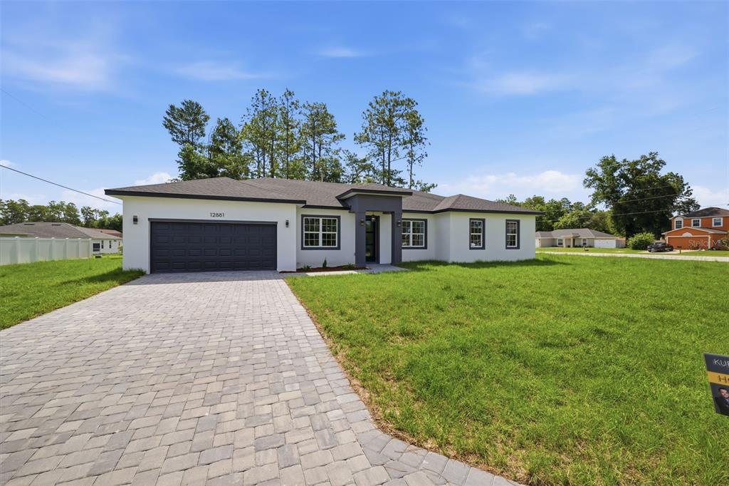 A modern single-story house with a white exterior, dark garage door, and paved driveway — 12881 SW 56TH TERRACE, OCALA, FL