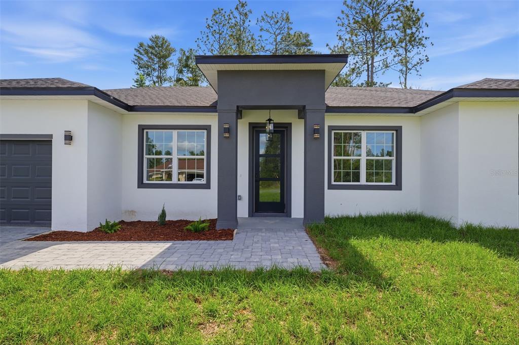 A modern single-story house with a white stucco exterior, dark gray trim, and a paved walkway — 12881 SW 56TH TERRACE, OCALA, FL