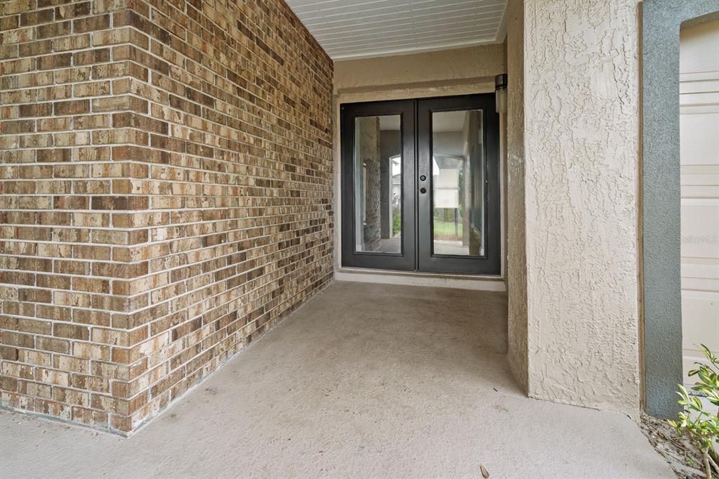 A covered entryway features a brick wall, a concrete floor, and dark double glass doors — 7437 PINEMOUNT DRIVE, ORLANDO, FL