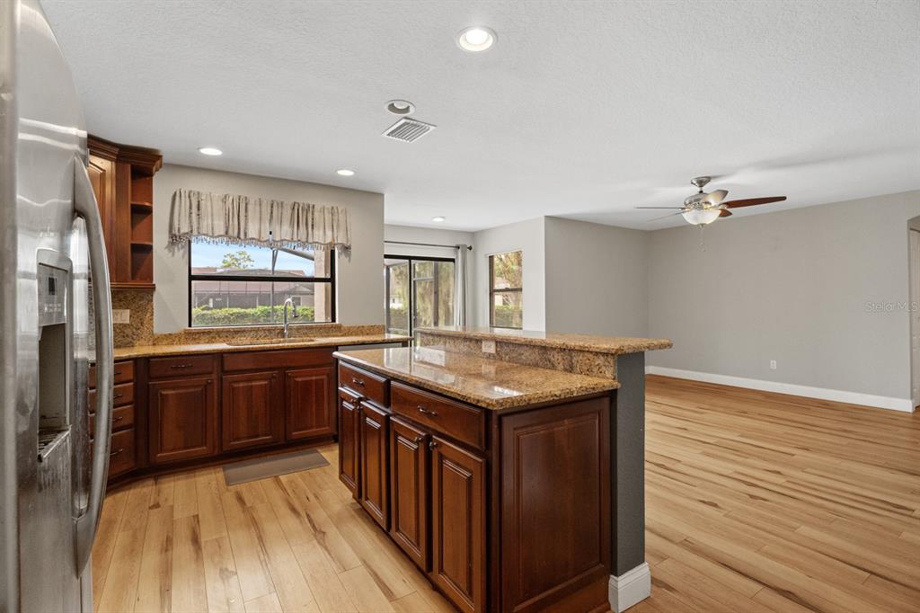 A kitchen with dark wood cabinets, granite countertops, and light wood flooring opens to a room — 7437 PINEMOUNT DRIVE, ORLANDO, FL