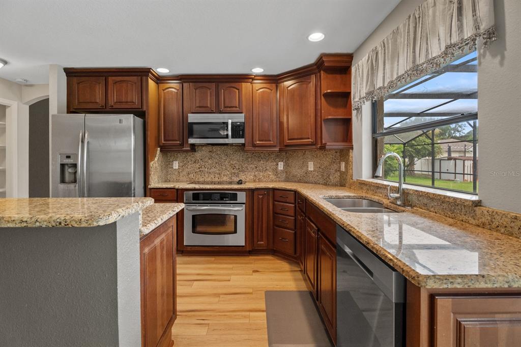 A kitchen with dark wood cabinets, granite countertops, stainless steel appliances, and light wood flooring — 7437 PINEMOUNT DRIVE, ORLANDO, FL