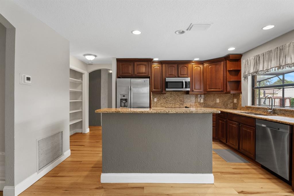 A kitchen features wood cabinets, granite countertops, stainless steel appliances, and a gray island — 7437 PINEMOUNT DRIVE, ORLANDO, FL