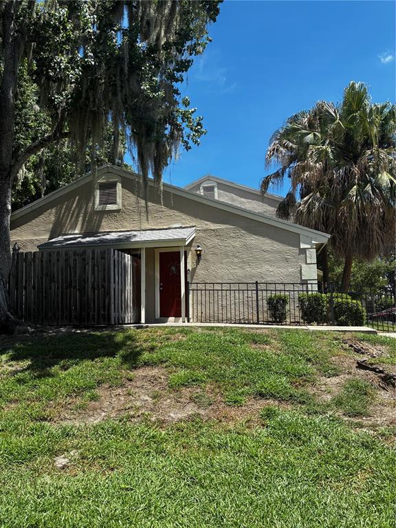 A tan, single-story building with a red door, wooden privacy fence, and surrounding landscaping — 1701 SE 24TH ROAD UNIT 201, OCALA, FL